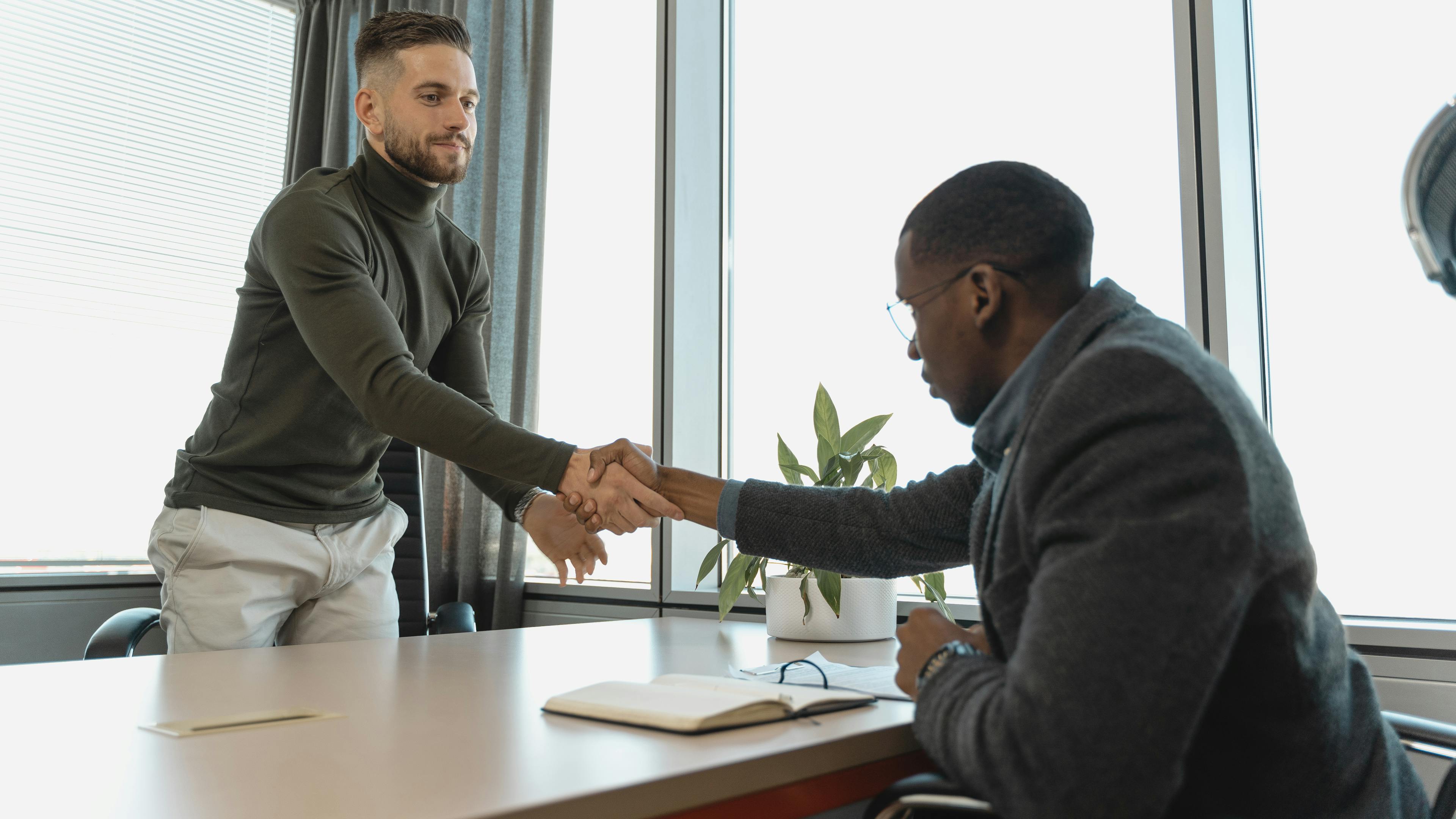 Two professionals shaking hands in a modern office during a hiring interview